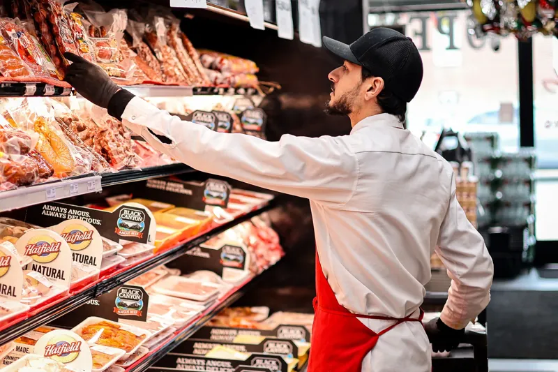 Un integrante del equipo de Victor’s, con delantal rojo, repone carnes empacadas en la vitrina refrigerada